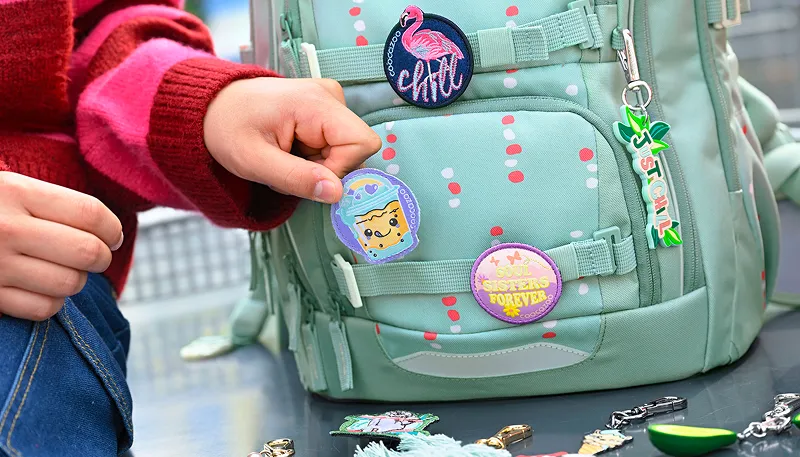 Kinderhand befestigt einen Patch zur individuellen Verzierung eines coocazoo Schulrucksacks.